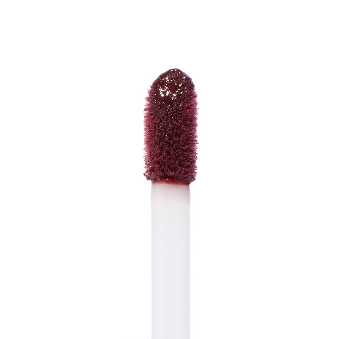 Doe-foot applicator coated in ColourPop Ultra Blotted Lip Canon Dr, a deep berry shade, captured in a macro close-up with saturated pigment on the fuzzy tip against a clean white background.