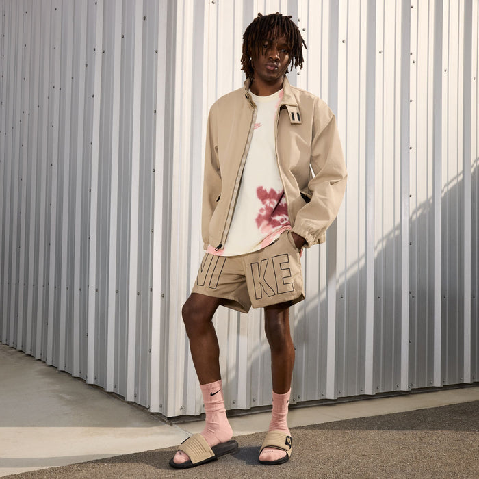 Men's tan slide sandals on feet, tan strap with black Nike logo and black sole