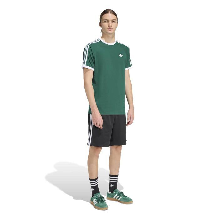 Men's green t-shirt worn with black athletic shorts; white three-stripe sleeve detailing