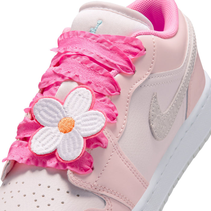 Youth sneaker close-up with pink ruffled strap and white flower applique with orange center