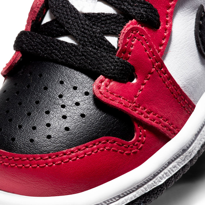Close-up of toddler sneaker upper: red leather, black strap, and perforated toe panel.