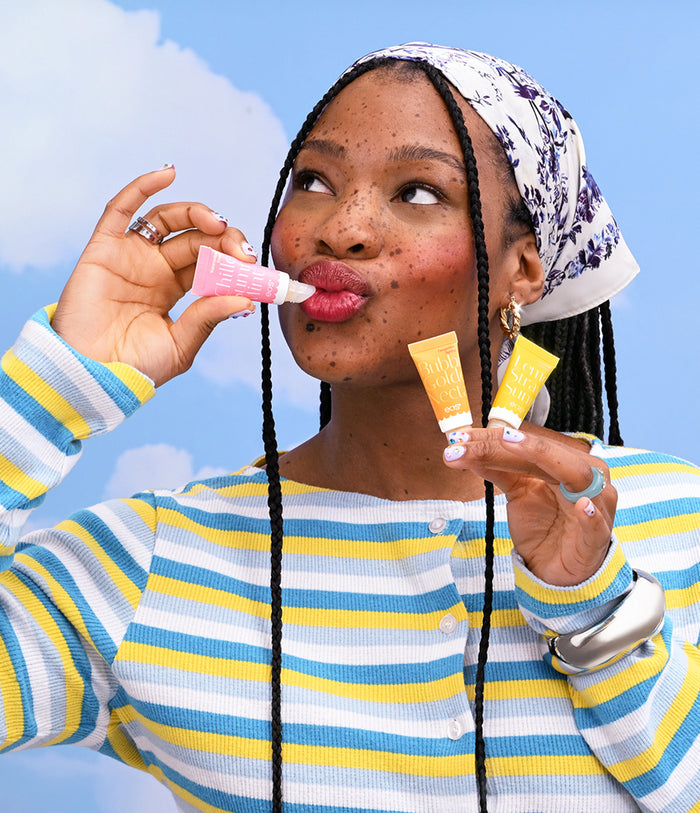 Woman applying lip balm against a blue sky background