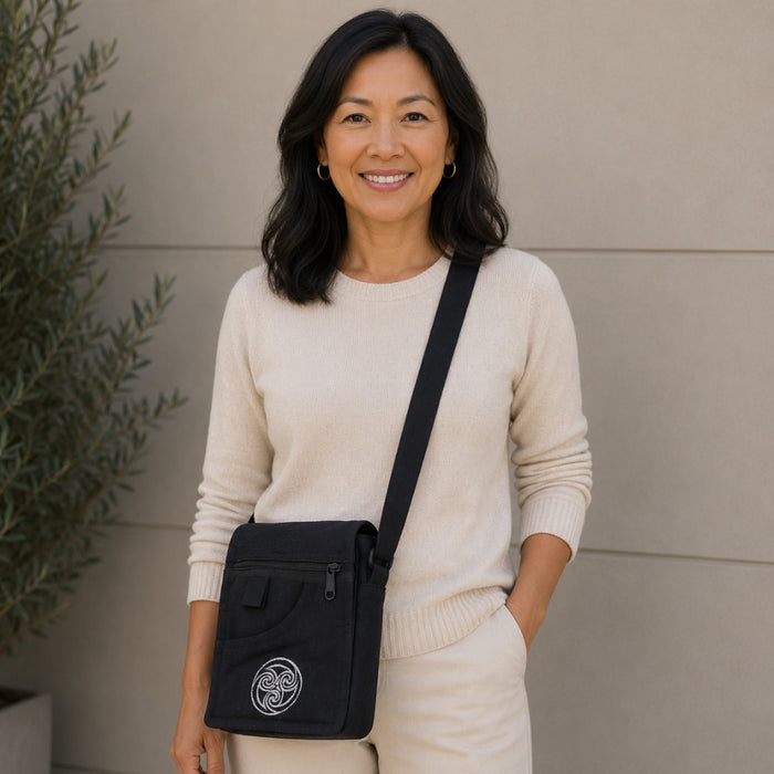 Woman wearing a beige sweater and pants with a black crossbody bag, standing against a neutral wall.