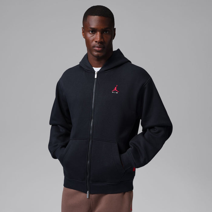 Men's black zip-up hoody with hood and red logo on left chest; front view on model.