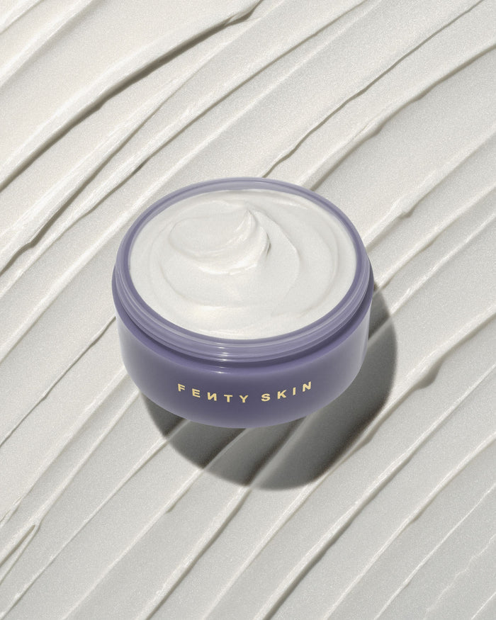 An open tub of Butta Drop Shimmering Whipped Oil Body Cream with Tropical Oils + Shea Butter on a textured smear background.
