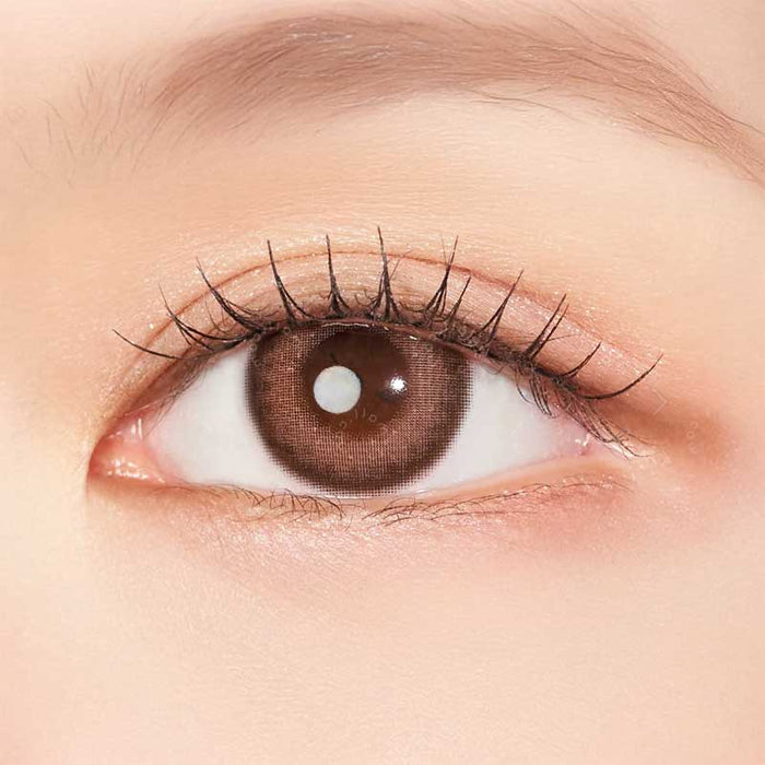 A close-up of a human eye with a light brown iris, long curled lashes, and natural makeup highlights the subtle effect of Clalen IRIS Pink Tulip (10pk) colored contacts by Clalen, suitable even for myopia prescriptions.
