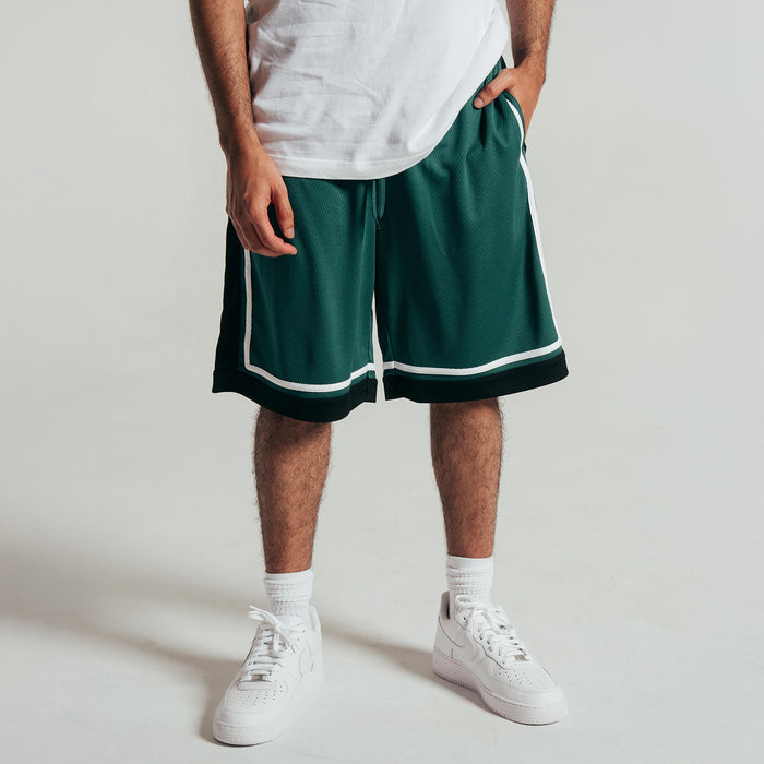 Men's green basketball shorts worn with white sneakers, black hem and white side piping