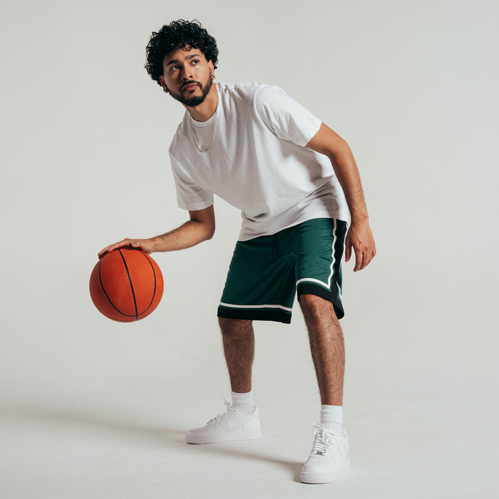 Men's green basketball shorts with black hem and white piping, worn mid-step with ball