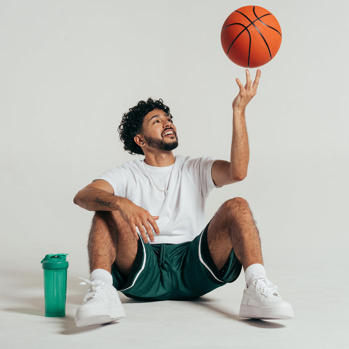 Men's green basketball shorts with black hem and white trim, elastic waistband while seated