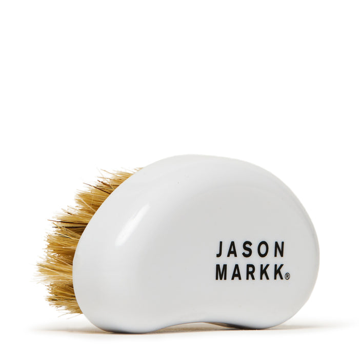 Round white soap bar with JASON MARKK logo and soft brush bristles behind