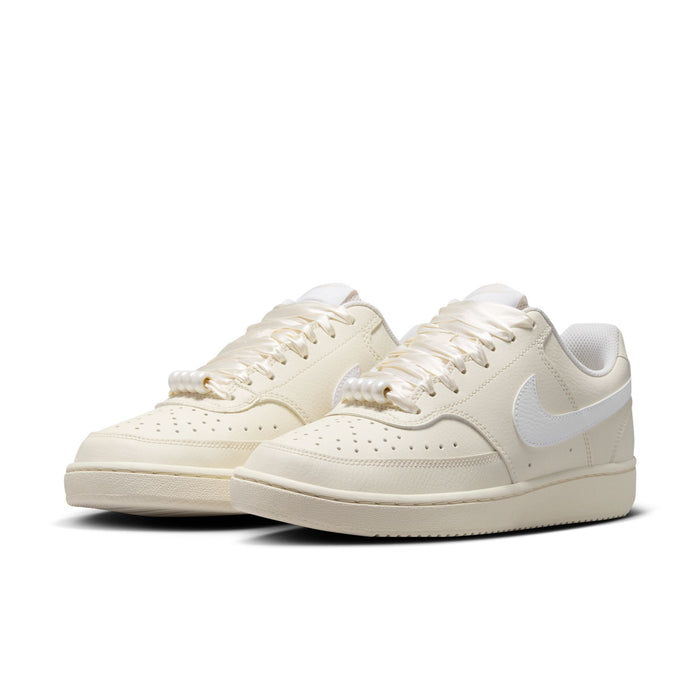 Pair of women’s low-top cream Nike sneakers with light blue swoosh and lace-up uppers