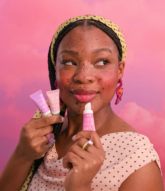 Woman holding three lip products against a pink background