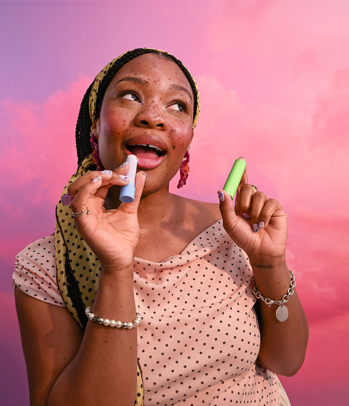 Woman holding colorful chalk pieces against a pink and purple cloud background