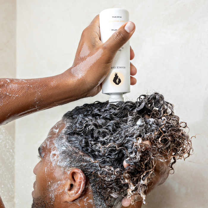 Person applying Bounce Curl shampoo to wet curly hair, creating lather on the scalp.