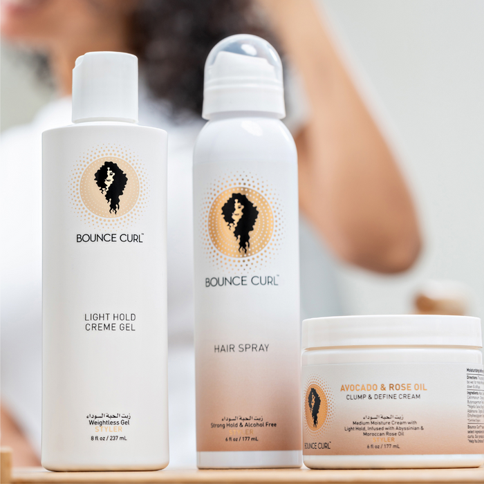 Bounce Curl haircare bottles and jar on a bathroom counter, person styling hair in the background.