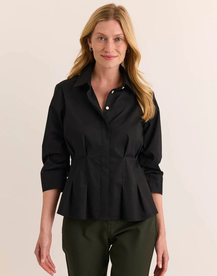 A woman with blonde hair is smiling at the camera while standing against a plain light background, wearing the HINSON WU - MARTINA 3/4 SLEEVE STRETCH POLISHED COTTON SHIRT IN BLACK paired with olive green pants.