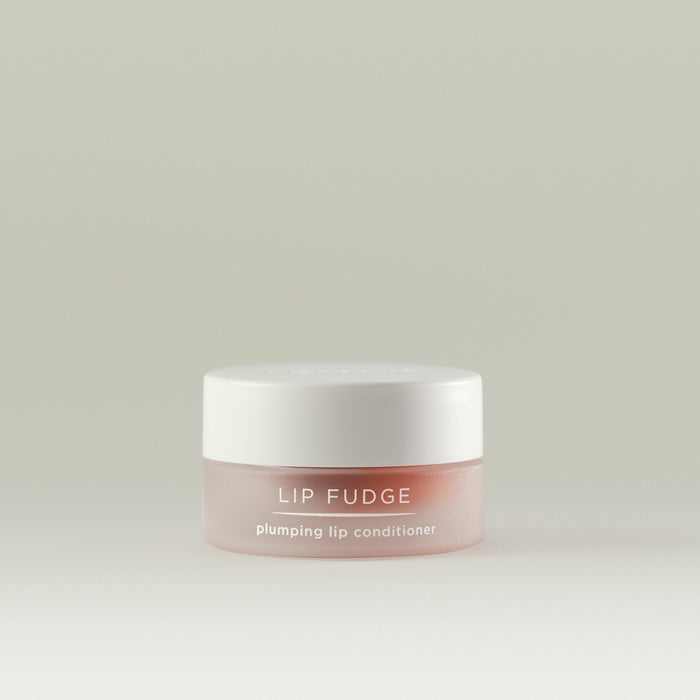 A small frosted rose-toned jar of Lip Fudge plumping lip conditioner with a white lid, shown against a soft, neutral background.