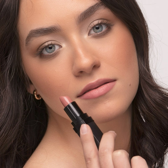 Woman wearing Demure Luscious Lipstick and holding the lipstick close to her lips with a neutral background