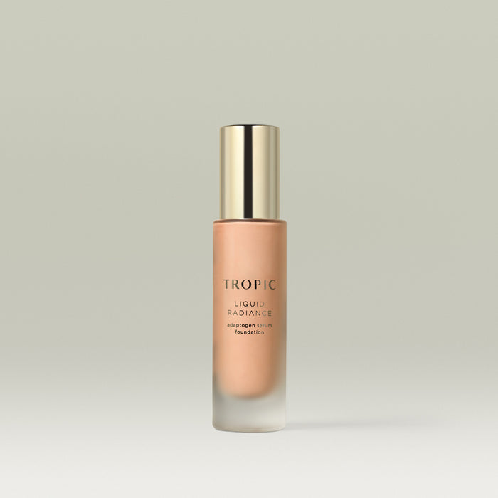 A frosted glass bottle of Tropic Liquid Radiance adaptogen serum foundation in shade 4 with a gold cap, standing upright against a soft neutral background.
