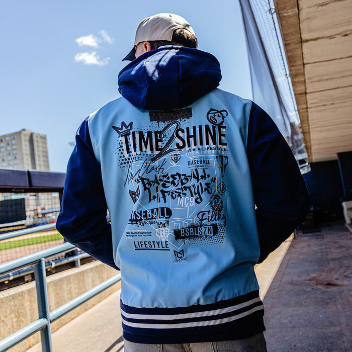 Person wearing a light blue and navy varsity jacket with text on the back, standing outdoors.