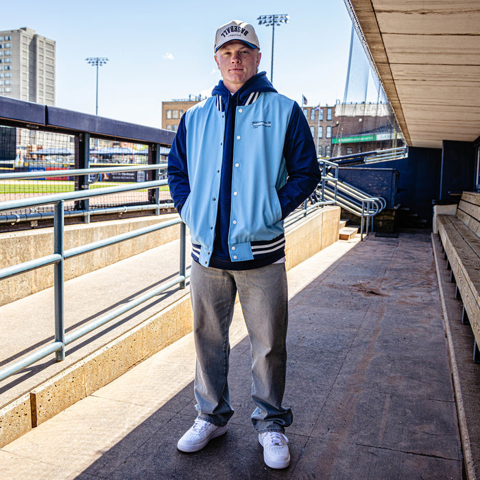 Person wearing a blue and black letterman jacket standing in a stadium setting