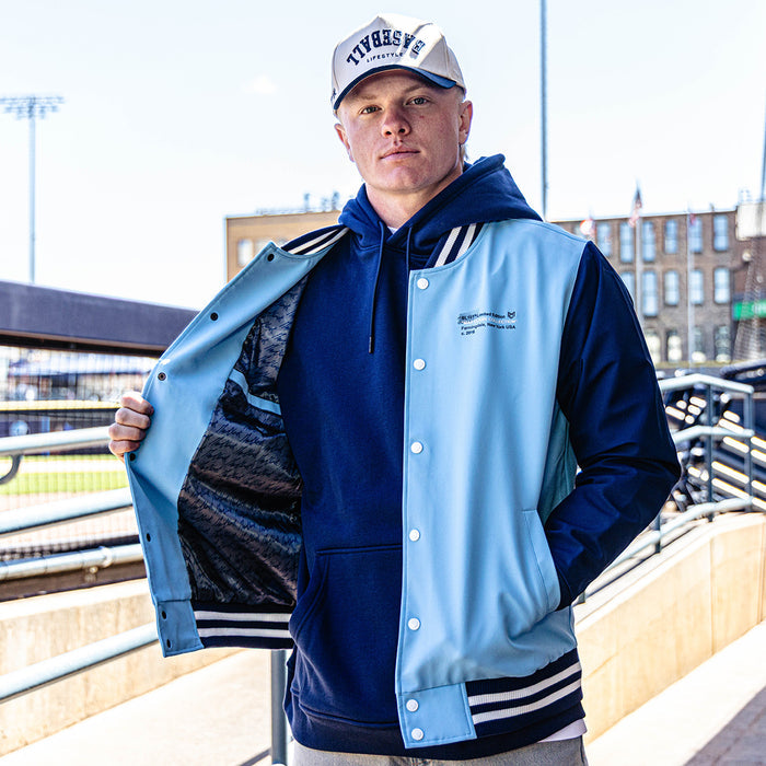 Person wearing a blue and light blue varsity jacket with a cityscape background