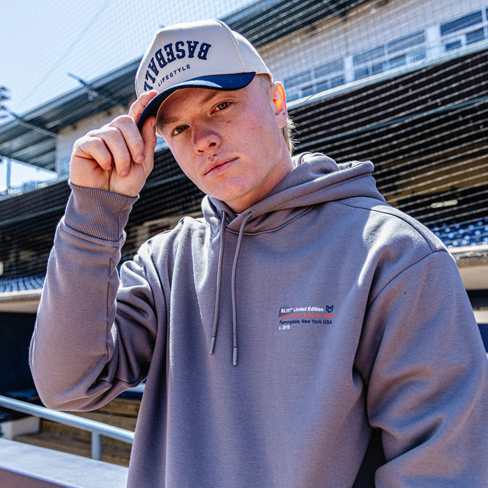 Man wearing a gray hoodie and cap with text, standing outdoors.
