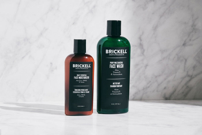 Brickell men's hair care products, including a shampoo and conditioner bottle, alongside product packaging and a yellow flower on a beige background.