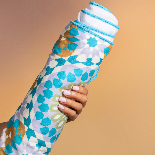 Woman holding a Bounce Curl micro fiber towel showcasing geometric patterns and bright colors.