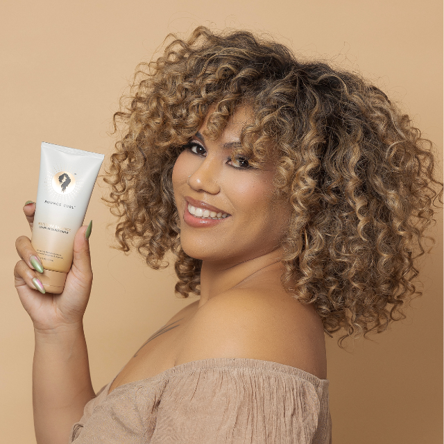 Woman with curly hair holding Bounce Curl Moisture Balance Leave-In Conditioner