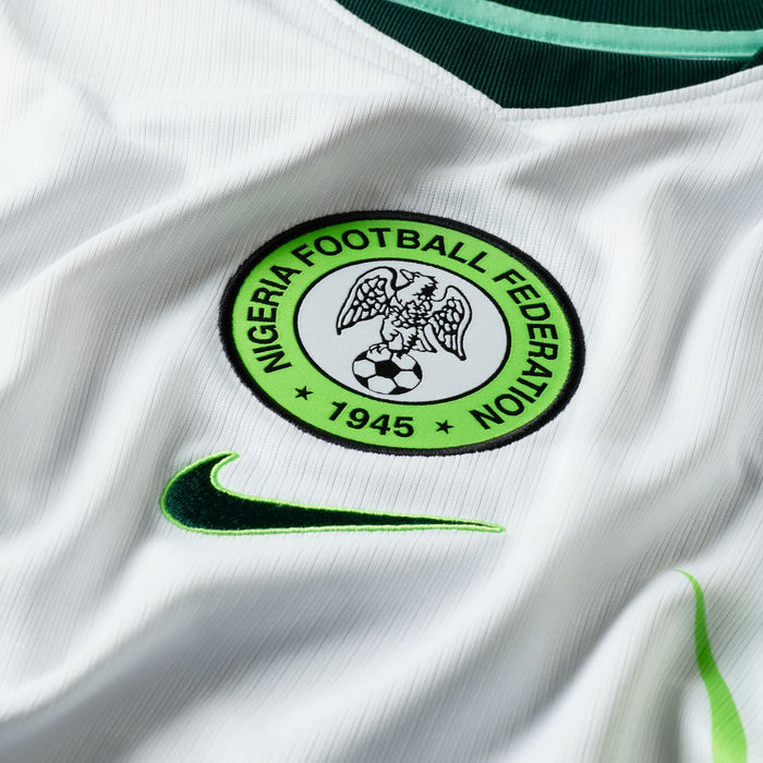 Round Nigeria Football Federation crest with 1945 and stars; Nike swoosh on white jersey.