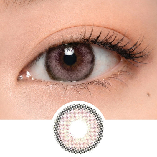 Close-up of a human eye wearing EyeCandys Pink Label Angel Pink lenses, showing their grayish-lavender tint. The lens design—a radial pattern with a lighter center—is displayed below the eye.