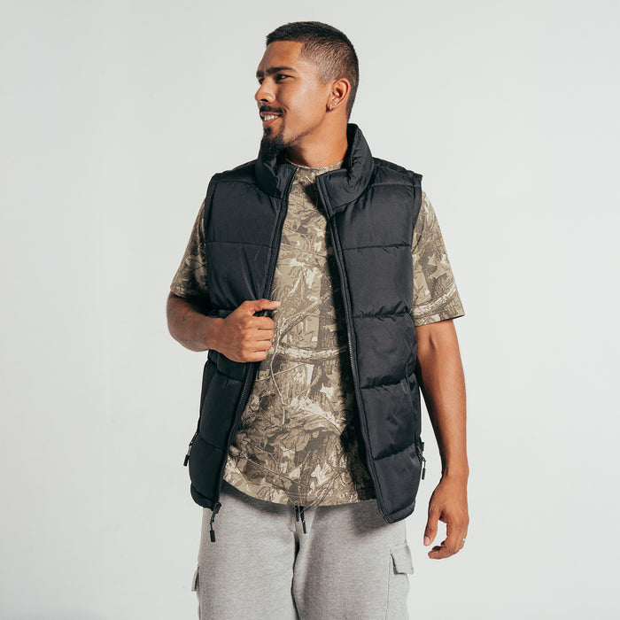 Black sleeveless quilted puffer vest worn over a t-shirt; front zipper.