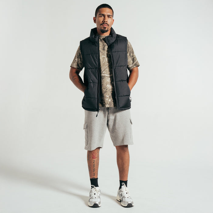 Black men’s padded puffer vest with zip front and stand collar; full outfit view.
