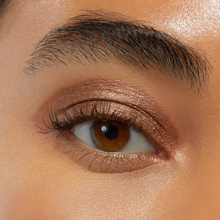 Brown eye wearing ColourPop Shadow Stix in Quokka, a shimmering warm bronze shade swept over the lid and softly blended into the crease, showcasing creamy metallic payoff in a close-up beauty swatch.