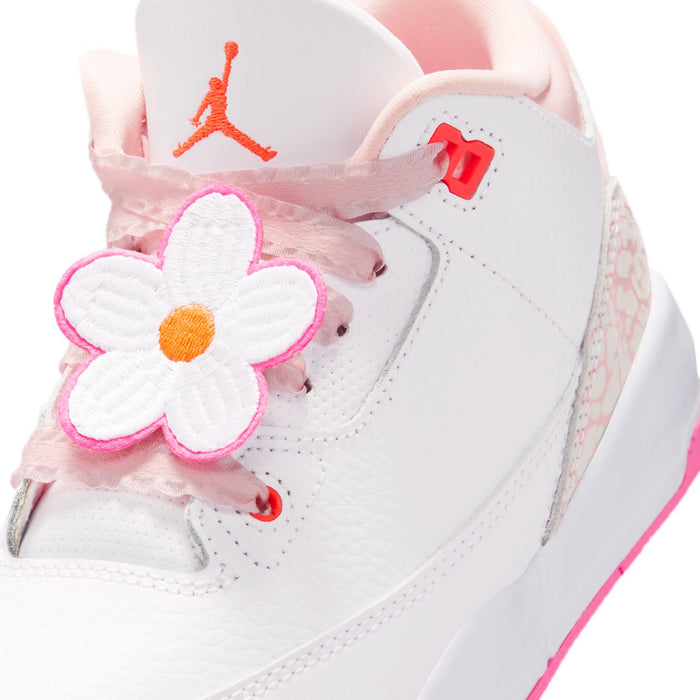 Kids' sneaker close-up: white upper with pink flower applique, orange Jumpman on heel.
