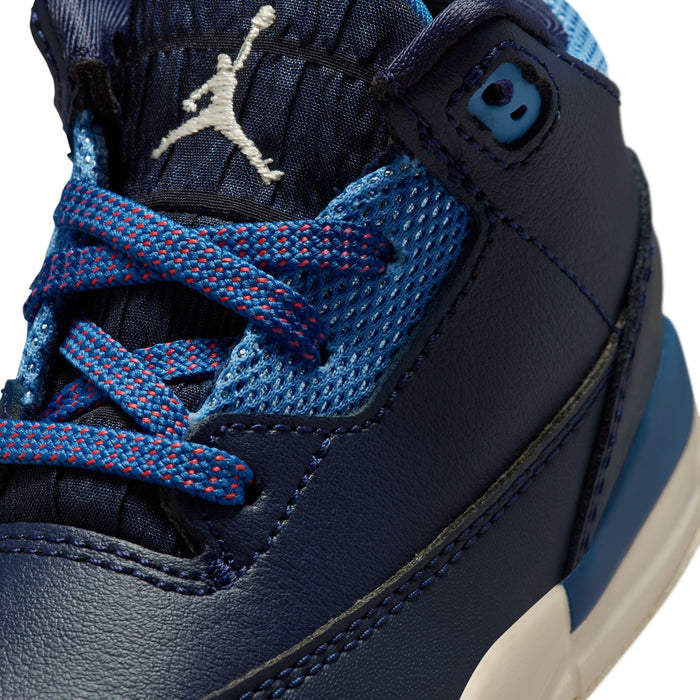 Close-up of toddler sneaker: navy leather, mesh detail, and red/blue braided laces