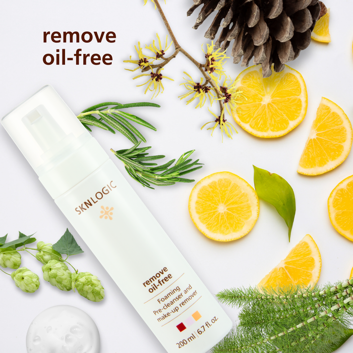 SKN128 SKNLOGIC Makeup Remover Oil Free 200ml | A bottle of SKINLOGIC Remove Oil Free foaming cleanser is displayed in a styled flat-lay composition on a white background, surrounded by natural ingredients including a pinecone, rosemary, green leaves, hops, and sliced oranges.