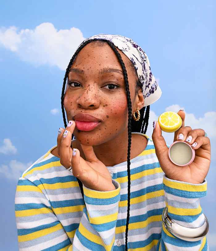 Woman holding a container of lip balm with a blue sky background