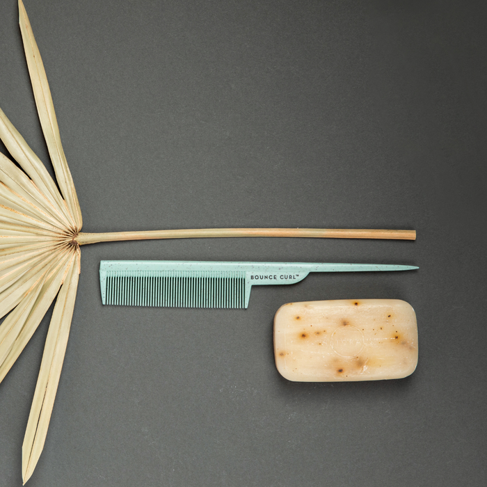 Bounce Curl mint-green comb with dried palm leaf, wooden hair stick, and soap on dark surface.