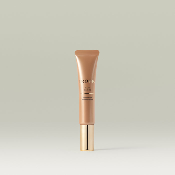A sleek bronze tube of Tropic Sun Glaze illuminating bronzing drops with a shiny gold cap, standing upright against a soft neutral background.