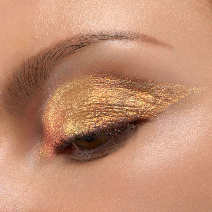 ColourPop Chrome Liquid Shadow in Sweetzer Ave swept across a closed eyelid, flashing molten gold with rose-copper shifts in a sharp wing, showcasing high-shine metallic finish and smooth, opaque payoff in a studio close-up.