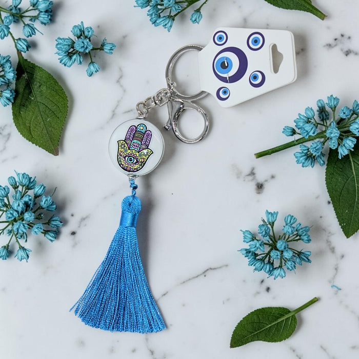 Keychain with blue tassel and decorative charm on a marble surface with flowers and leaves.