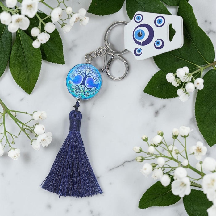 Blue tassel keychain with decorative element on a marble surface with flowers and leaves.