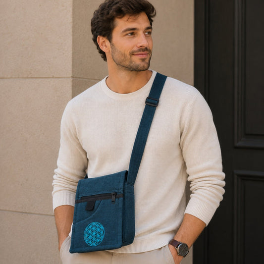 Man wearing a white sweater with a blue crossbody bag featuring a symbol on a beige wall.