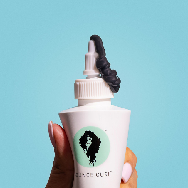 A hand squeezing a Bounce Curl product out of the bottle