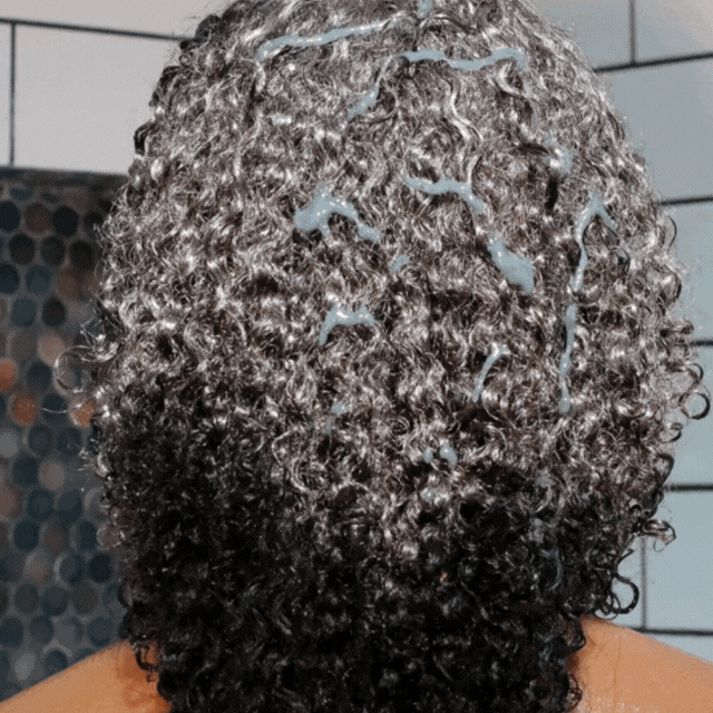 GIF of a person running product through curly hair with their hands