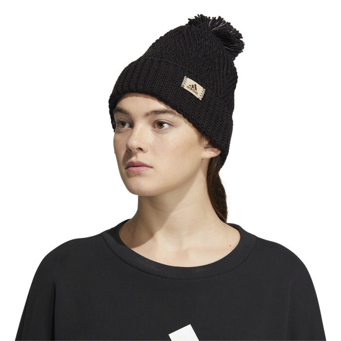 Black knit pom-pom beanie worn by model, small adidas logo patch on front