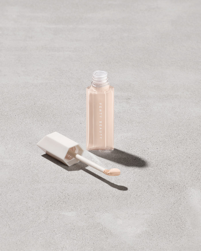 Open bottle of Fenty Beauty We're Even Hydrating Longwear Concealer with doe foot applicator in shade 125c on a concrete background.
